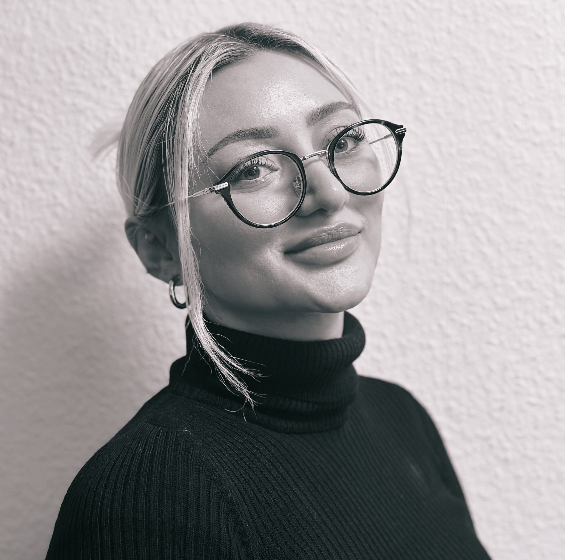 Auf einem Schwarzweißfoto lächelt eine Frau mit Brille und schwarzem Rollkragenpullover.