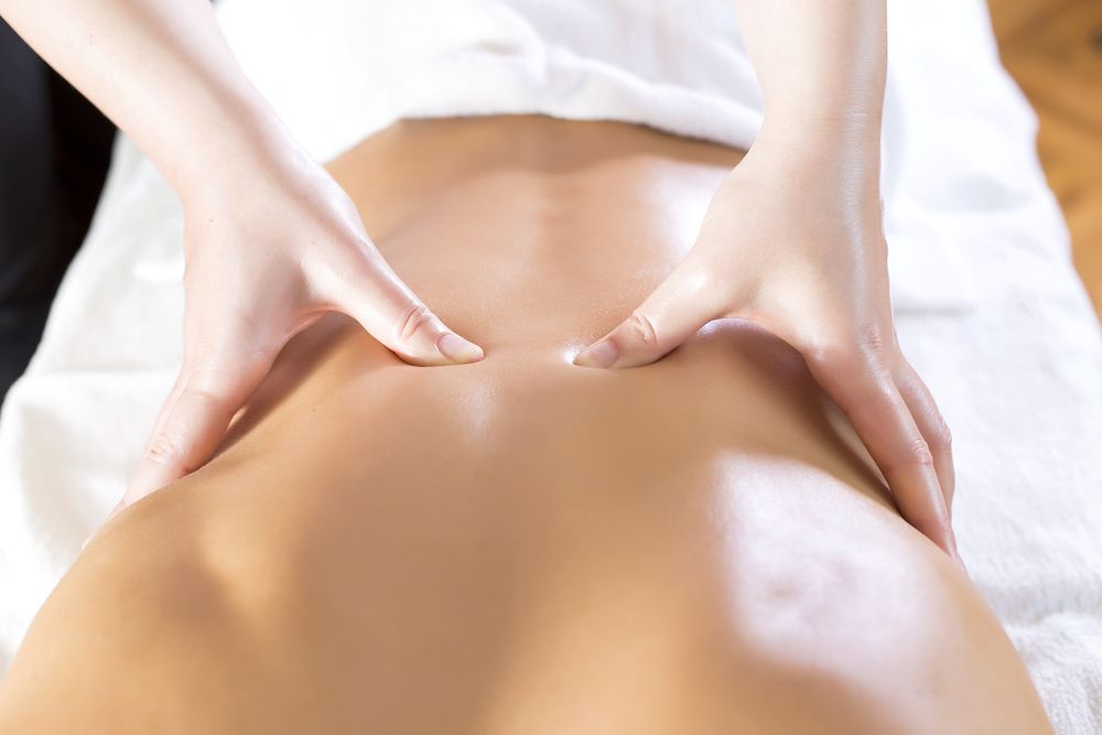 Manos masajeando la parte baja de la espalda de una persona durante un tratamiento de spa.
