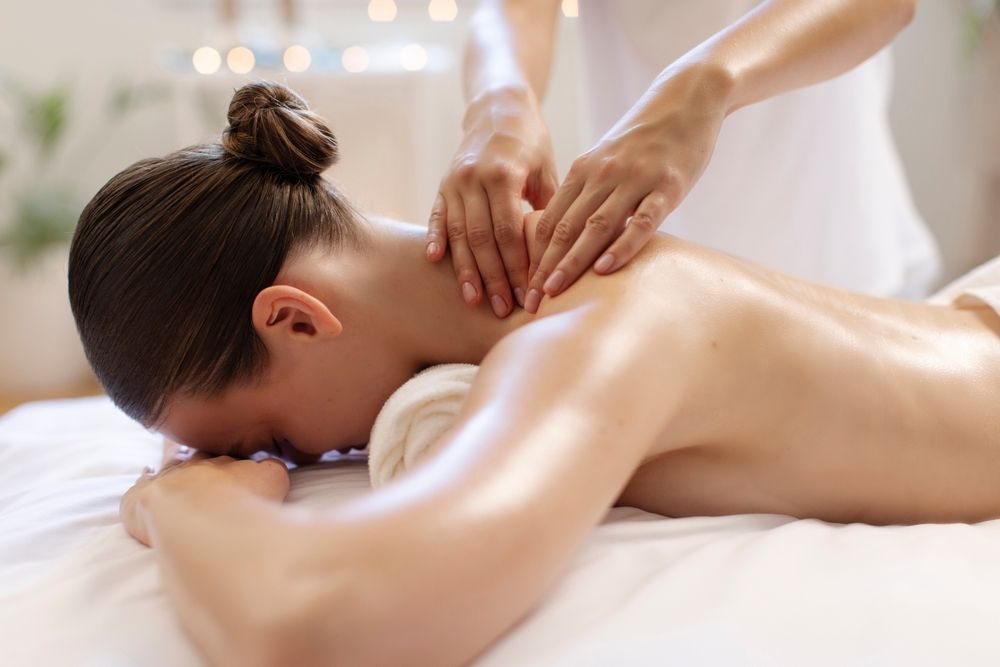 Mujer recibiendo un masaje de espalda en una camilla de spa, con manos presionando su cuello y hombros.