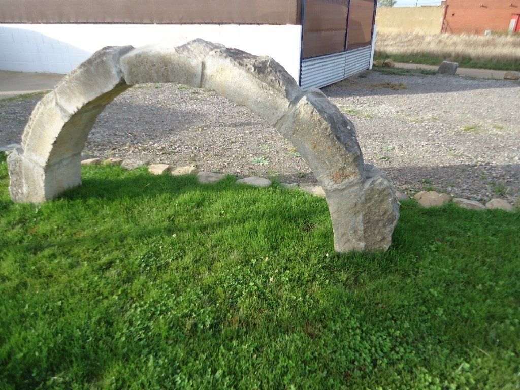 Un arco de piedra está sentado en el césped frente a un edificio.