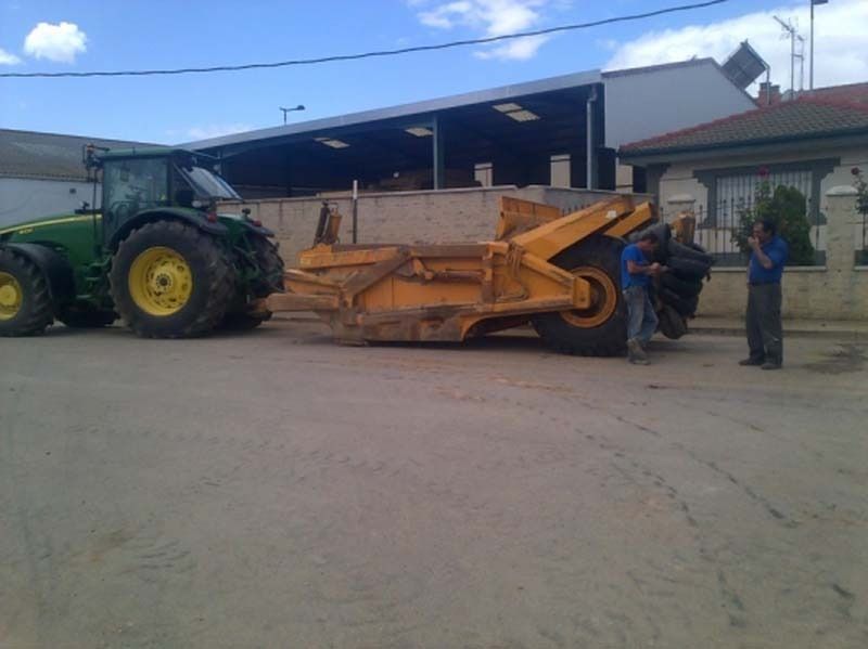 Un tractor John Deere está estacionado junto a un gran raspador amarillo.