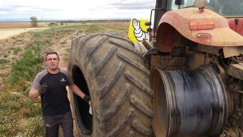 Un hombre está parado al lado de un neumático grande en un tractor.