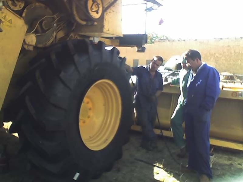 Dos hombres con overoles azules están parados junto a un neumático de tractor grande.