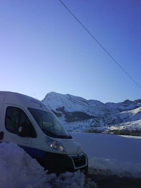 Una furgoneta blanca está aparcada en la nieve con montañas al fondo.