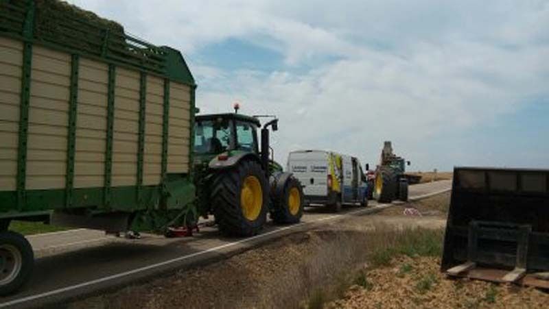 Un tractor está tirando de un remolque lleno de heno por una carretera.