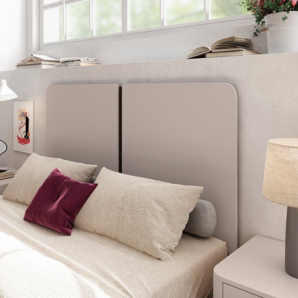 Dormitorio moderno con cama beige, almohadas, lámpara y repisa de ventana con plantas y libros.