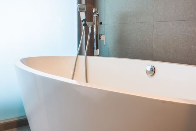 Bañera moderna blanca independiente con grifería cromada en un baño alicatado.