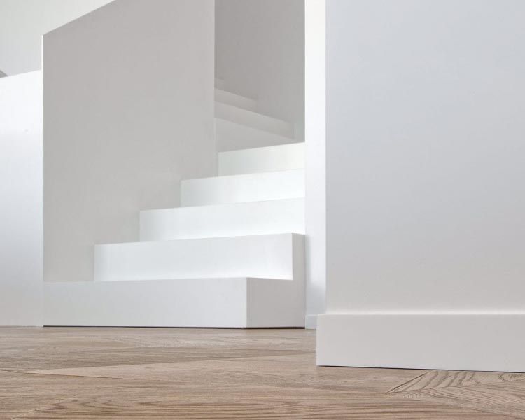 Una escalera blanca en una habitación con piso de madera y paredes blancas.