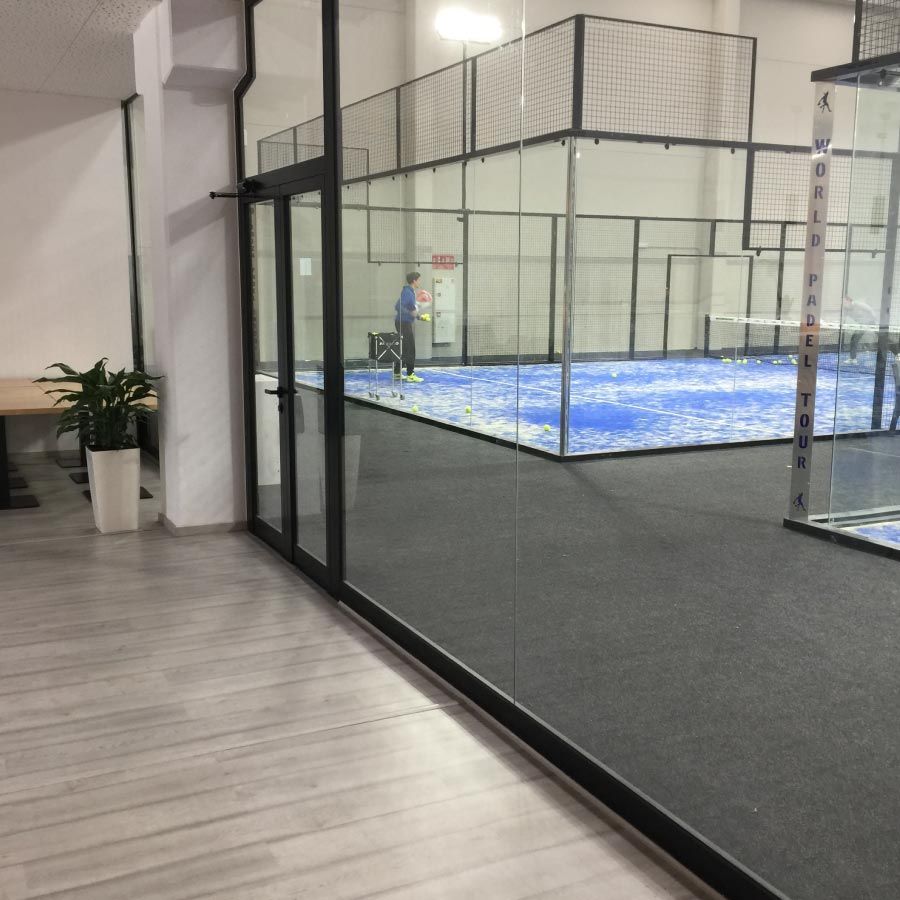 Un hombre está de pie en una habitación con una cancha de pádel al fondo.