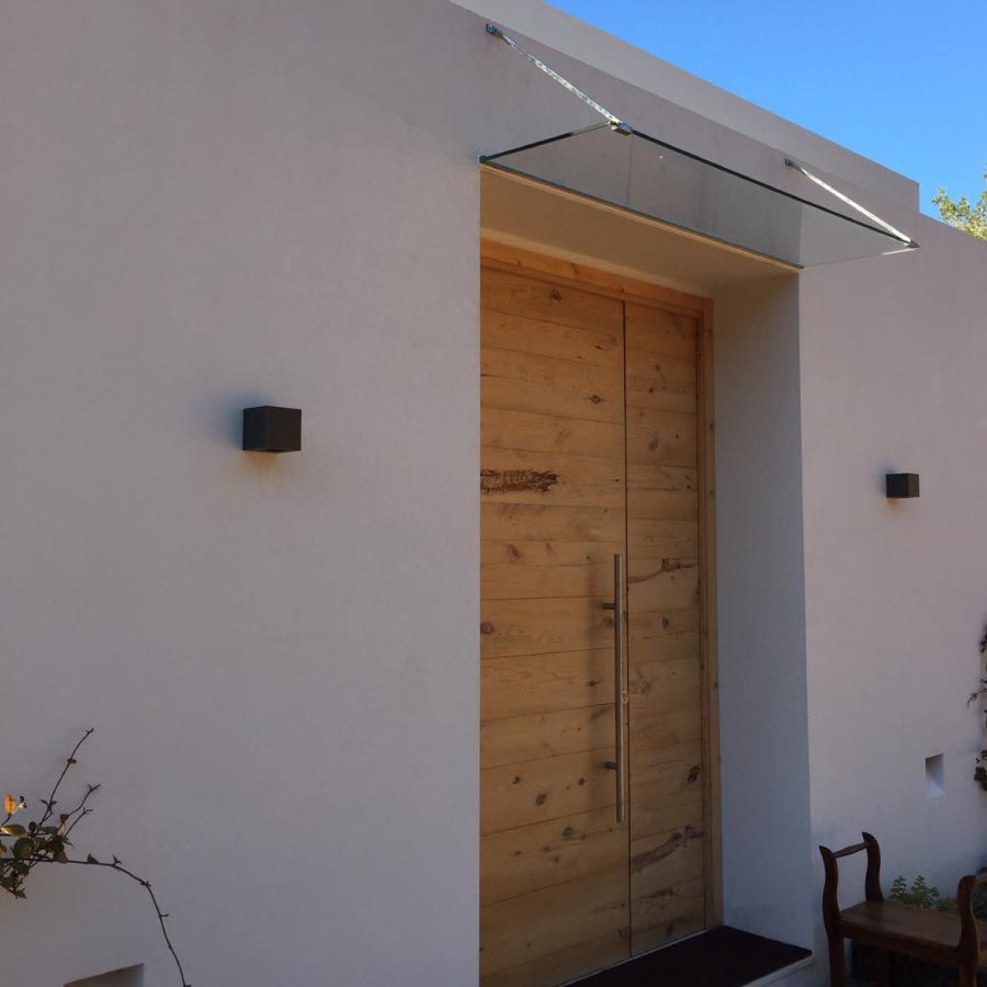 Un edificio blanco con una puerta de madera y una marquesina de vidrio.