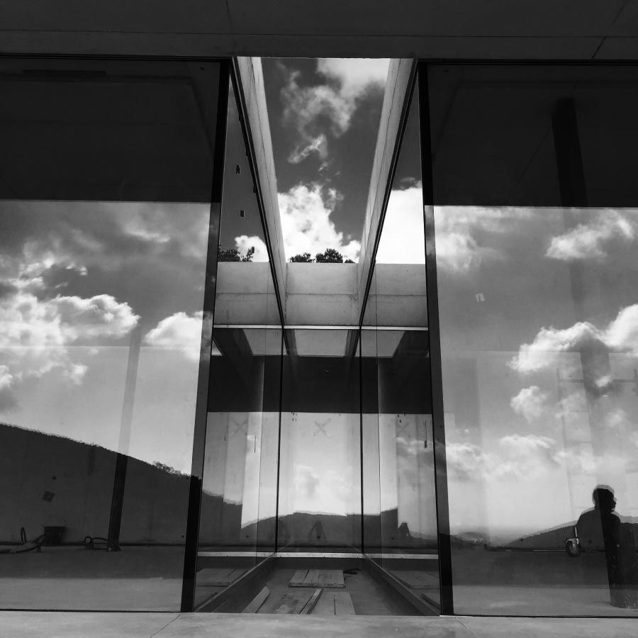 Una fotografía en blanco y negro de un edificio con nubes reflejadas en las ventanas.