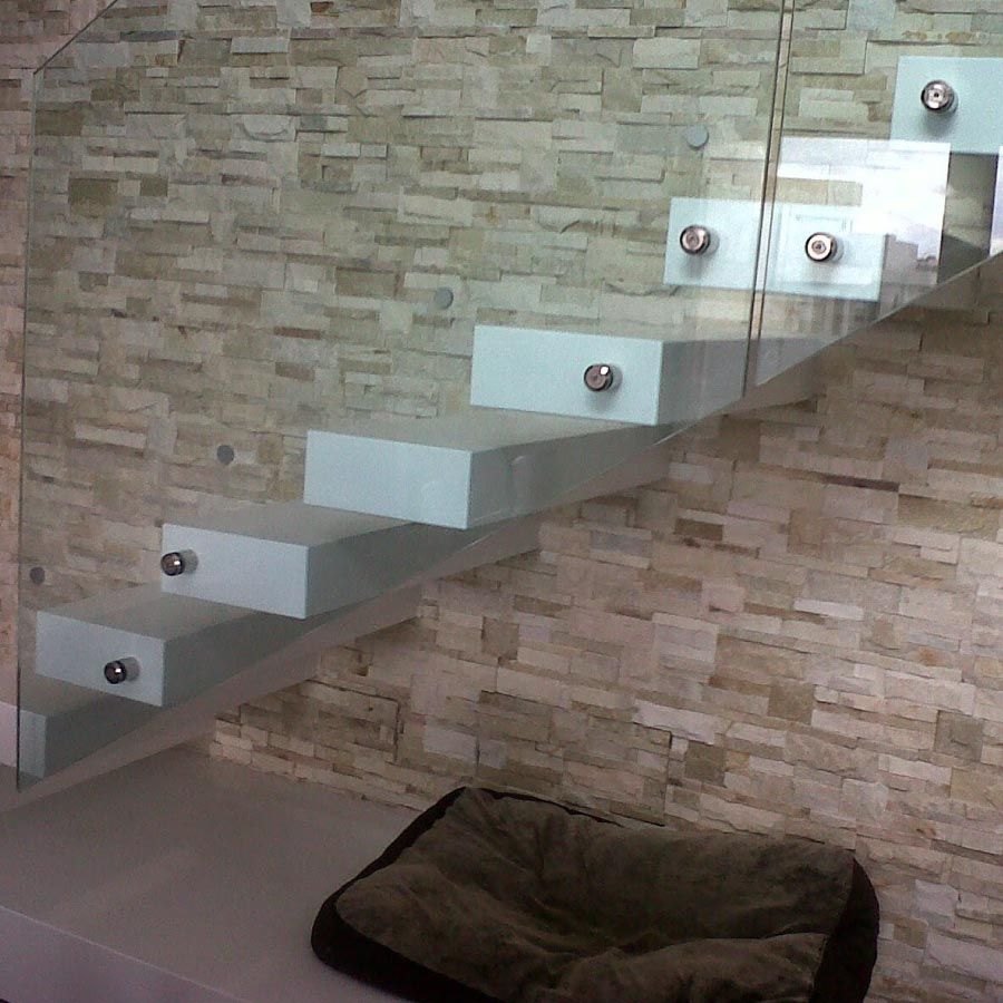 Una escalera con barandilla de cristal y una pared de ladrillo detrás de ella.