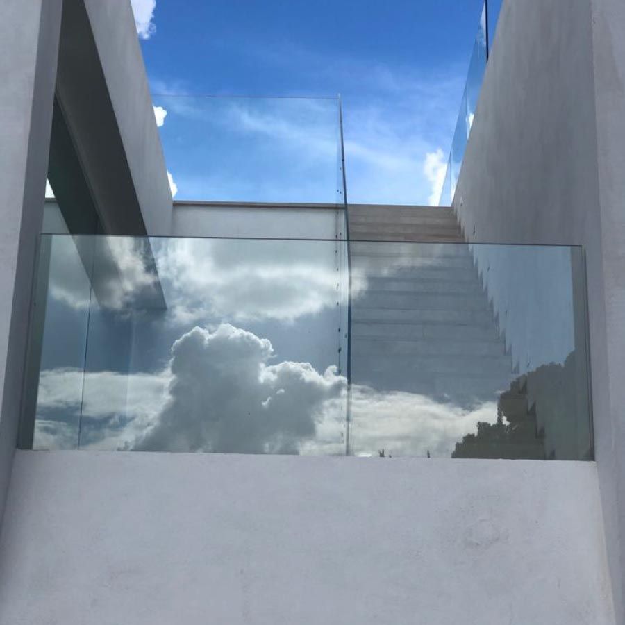 Un balcón con barandilla de cristal y escaleras que conducen a un cielo azul.