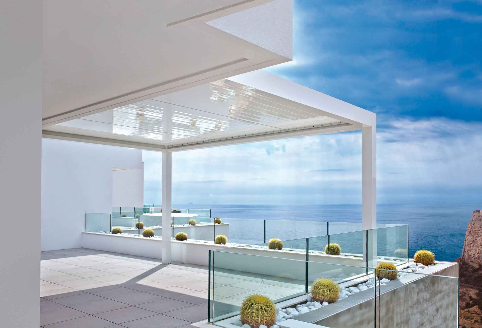 Un balcón con pérgola y barandilla de vidrio con vista al mar.