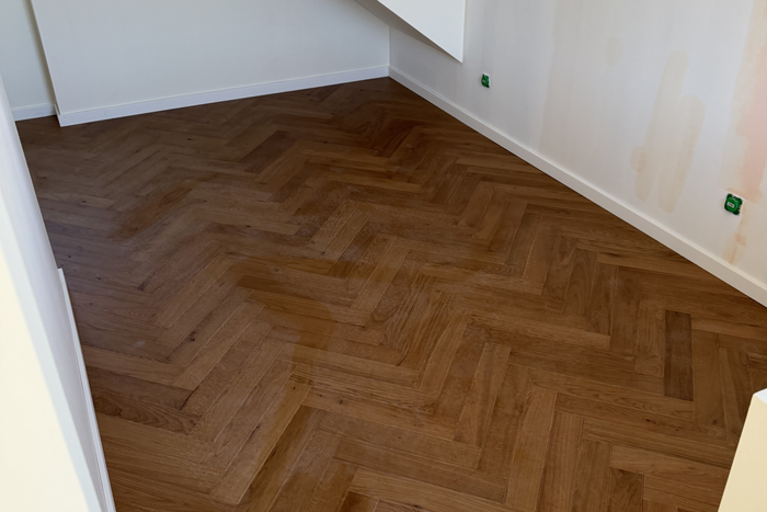 Coin d’une pièce vide avec un parquet foncé à chevrons et des murs blancs