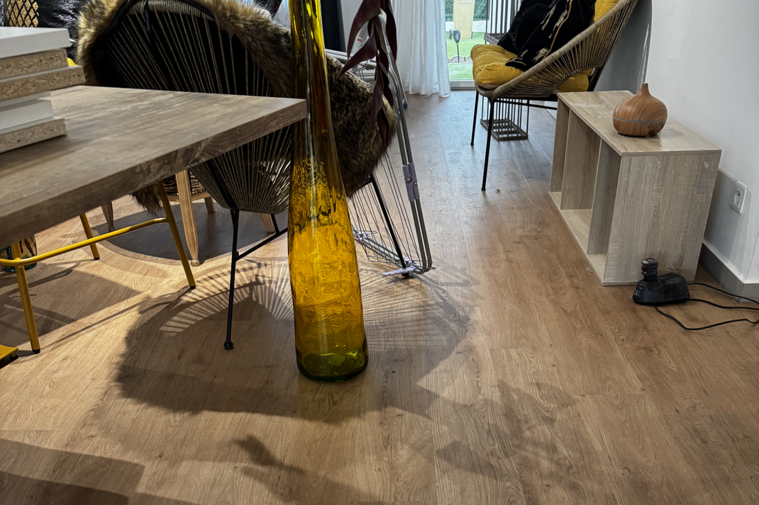 Des tables en bois, des chaises en osier, un vase jaune et une banquette sur un parquet en PVC.