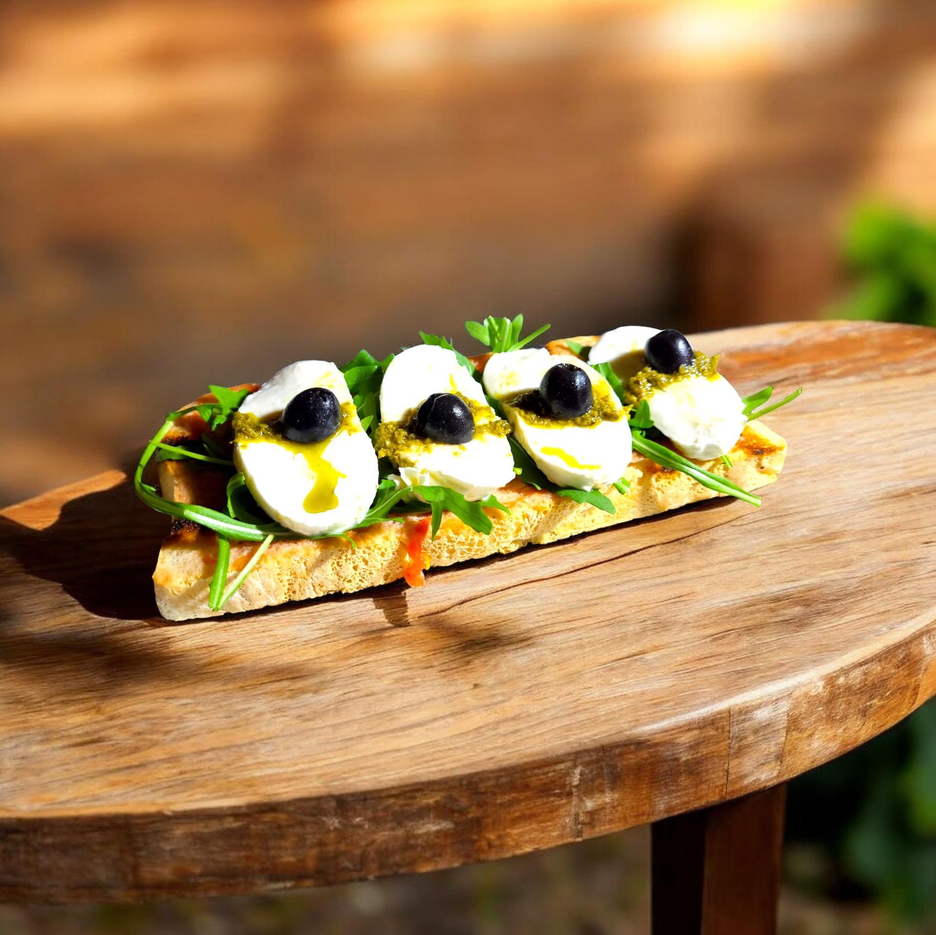 Una rebanada de pan tostado cubierta con mozzarella, pesto, verduras frescas y aceitunas negras sobre una superficie de madera.