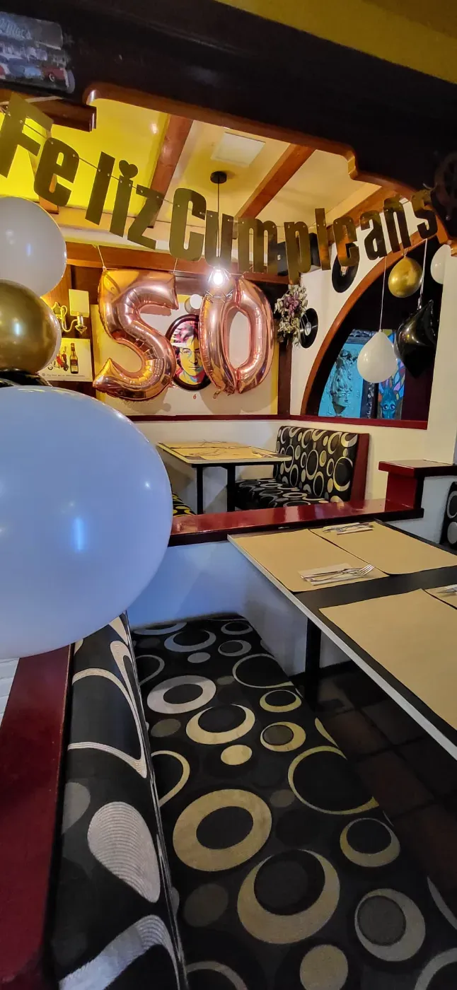 Un cóctel con una rodaja de naranja y una flor comestible junto a una botella de cerveza sobre un posavasos