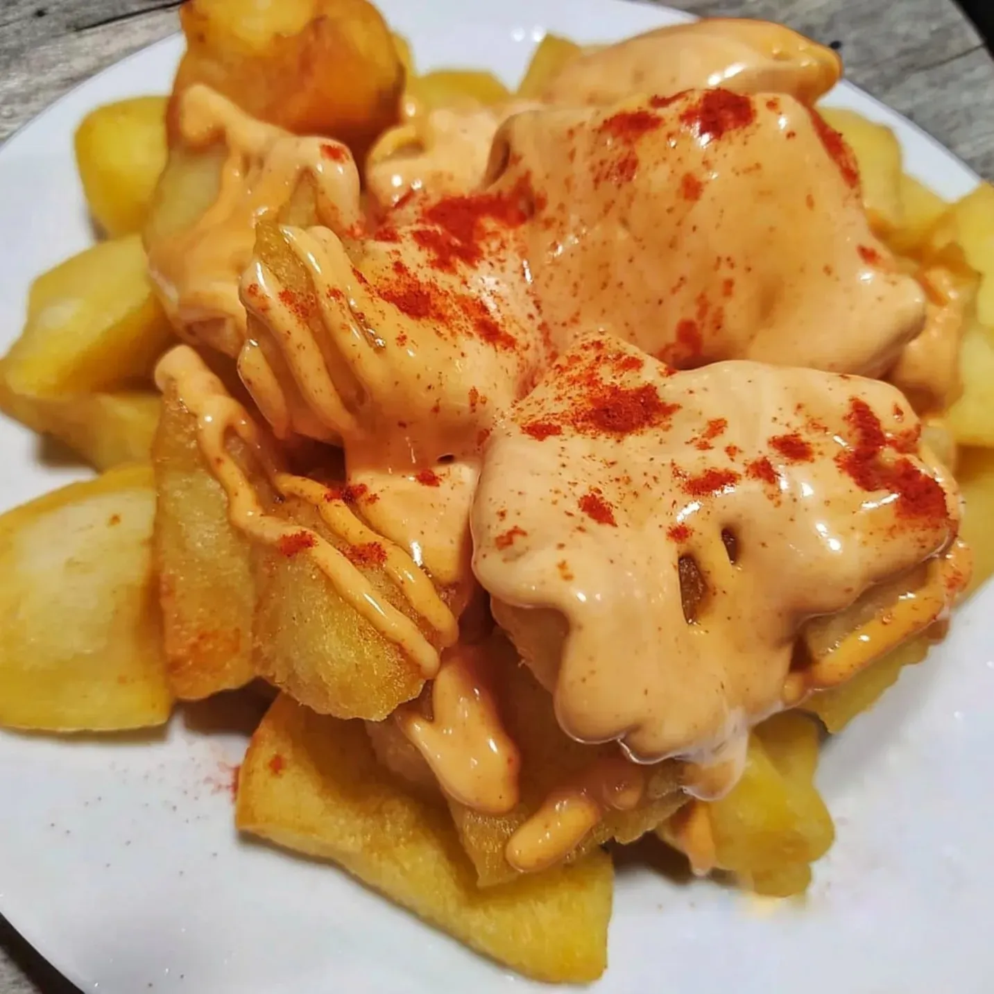 Un plato de cubos de patata fritos y dorados, cubiertos con una salsa cremosa de naranja y espolvoreados con pimentón rojo.