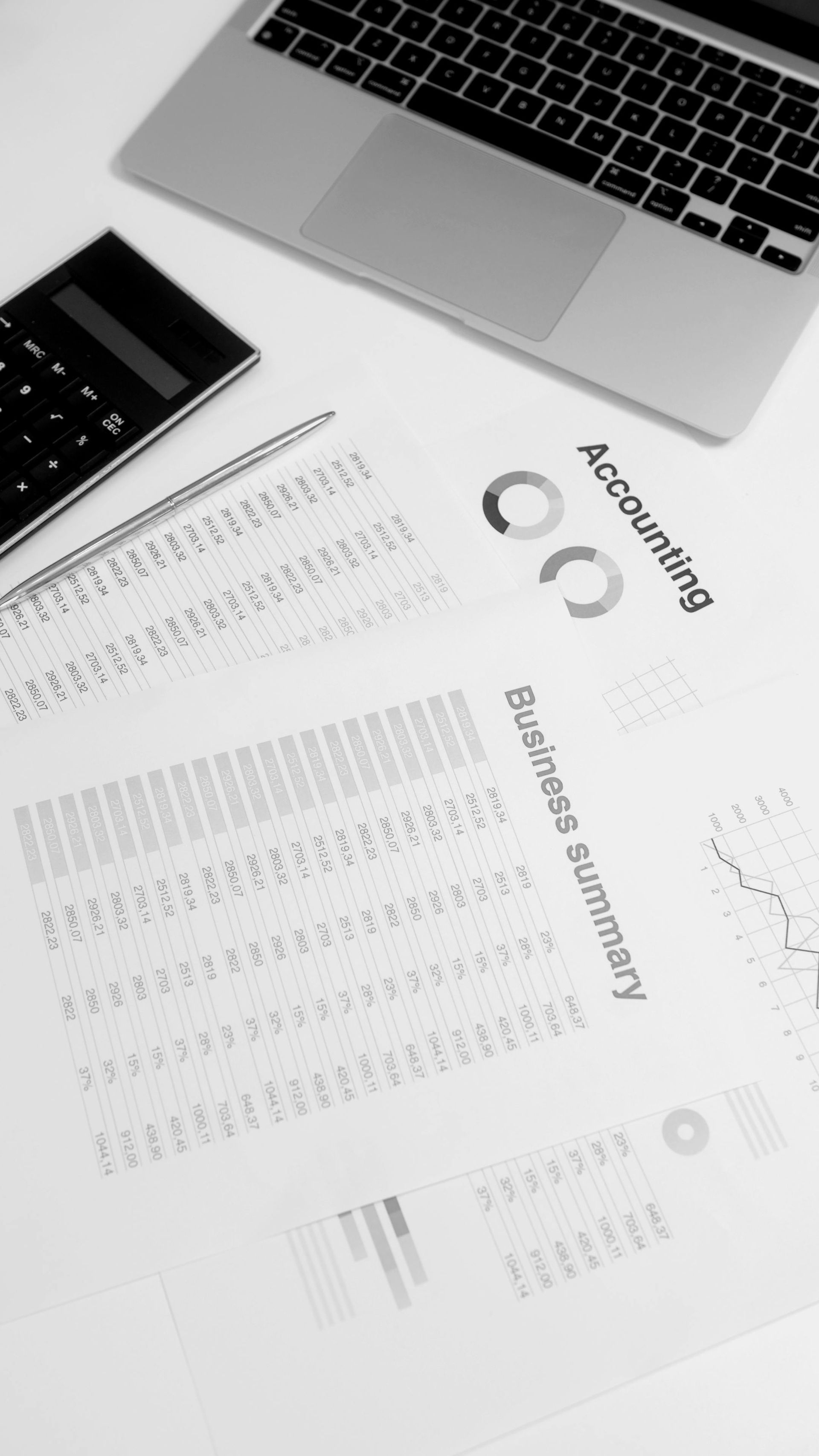 Sobre una superficie blanca, descansan un ordenador portátil, una calculadora y un documento resumen de negocios