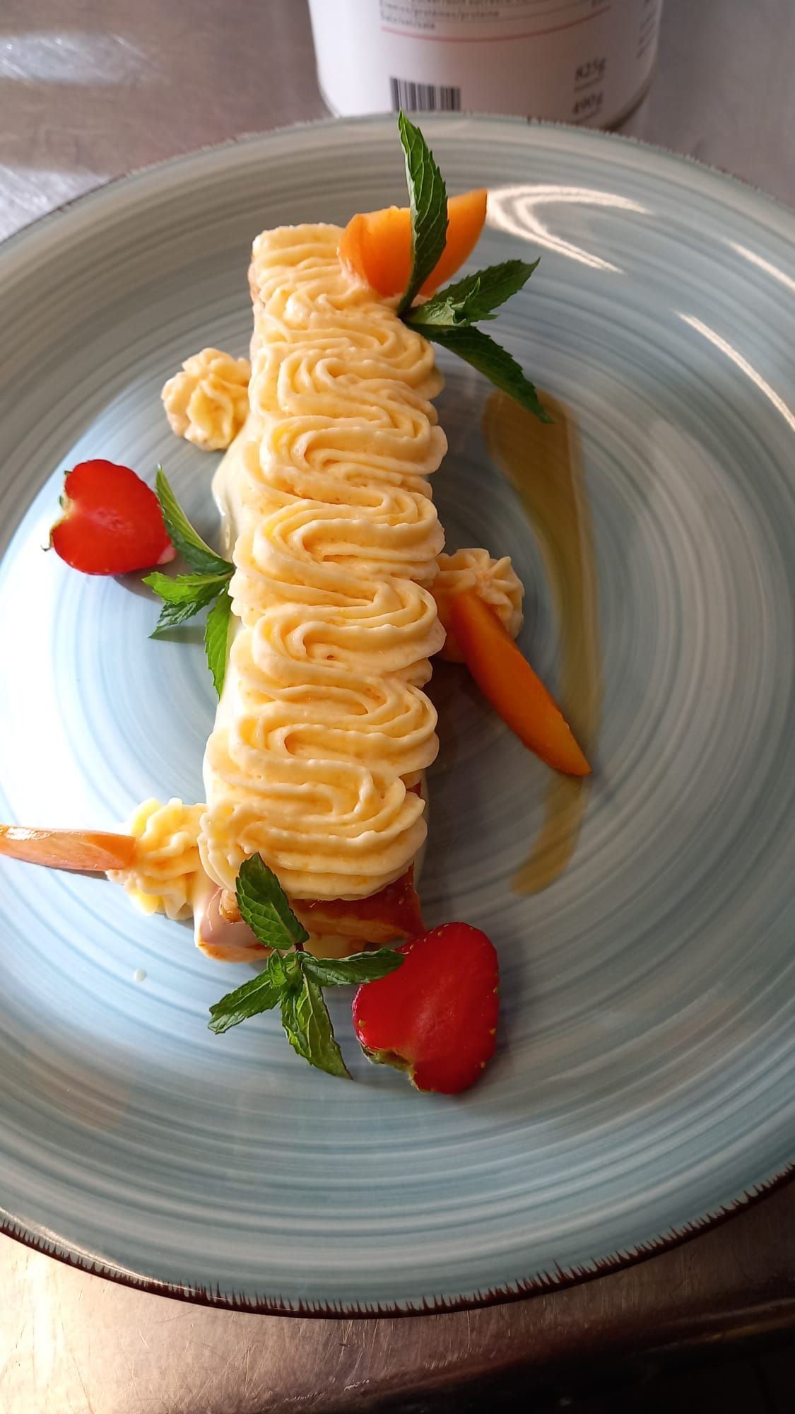 Ein Dessertteller mit aufgespritzter Sahne, Erdbeeren und Minze auf einem blaugrauen Teller.