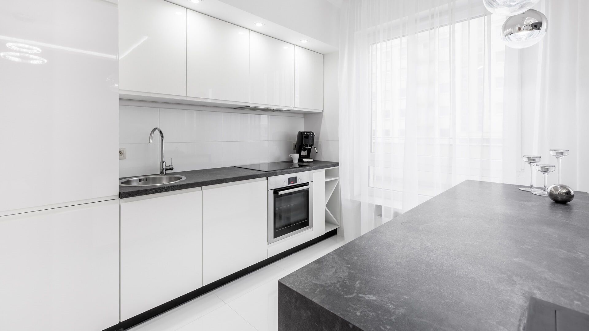 Uma foto em preto e branco de uma cozinha com armários brancos e uma bancada preta.