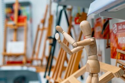 Puinen taiteilijan mannekiini poseeraa kädet ylhäällä ja seisoo sumean taidetarvikekaupan etualalla maalaustelineiden kanssa.