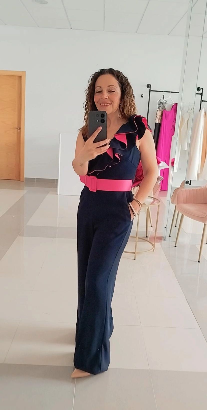 Mujer con mono azul marino con cinturón rosa y volantes, tomándose una selfie frente al espejo.