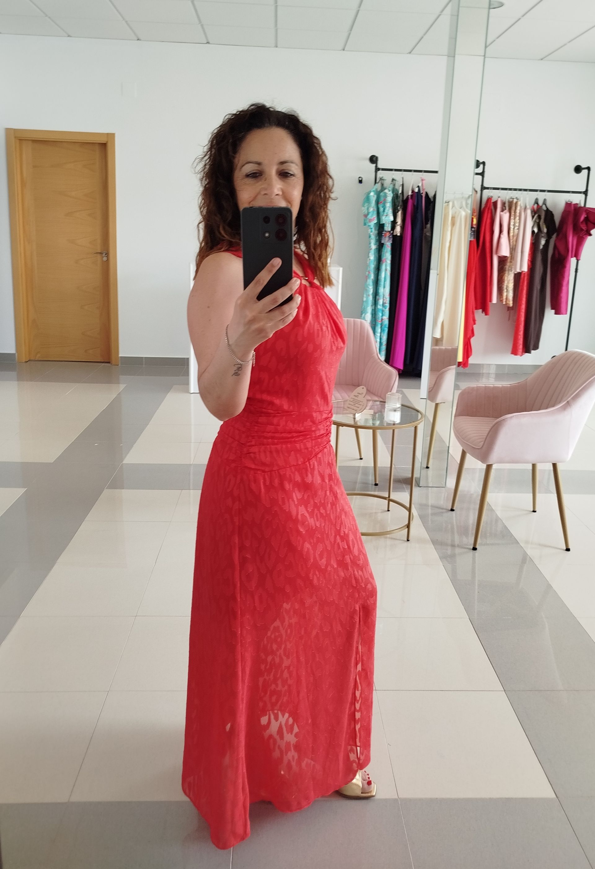 Mujer con un vestido formal rojo tomándose una selfie en una tienda.