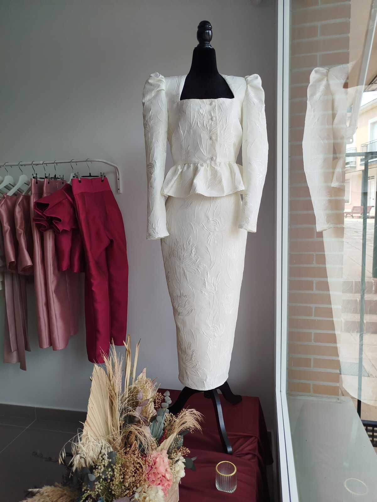 Vestido de encaje blanco sobre un maniquí, en un escaparate. Presenta escote cuadrado, top peplum y falda tubo.