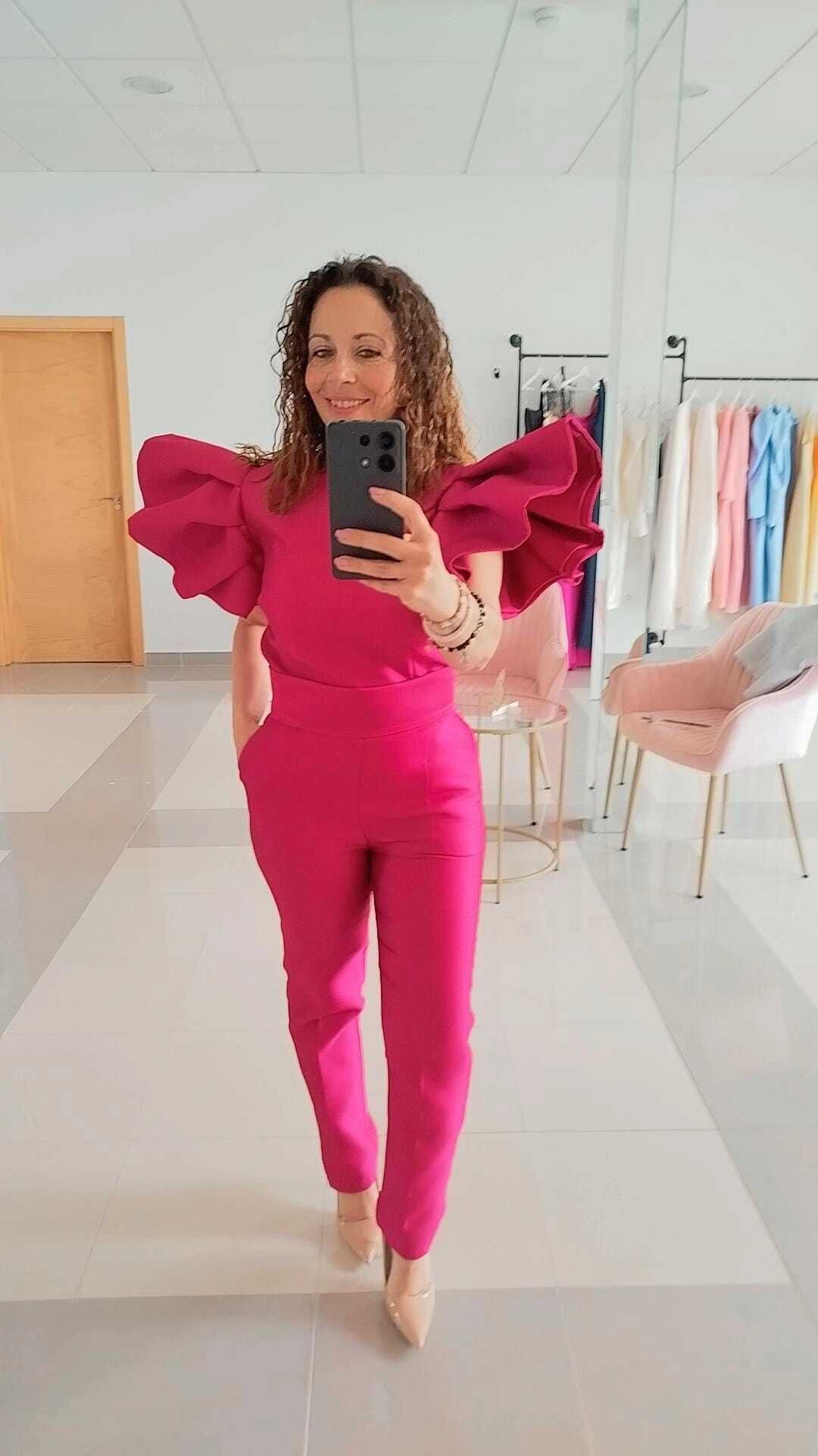 Una mujer con un mono fucsia con mangas con volantes posa en una habitación luminosa con un espejo.