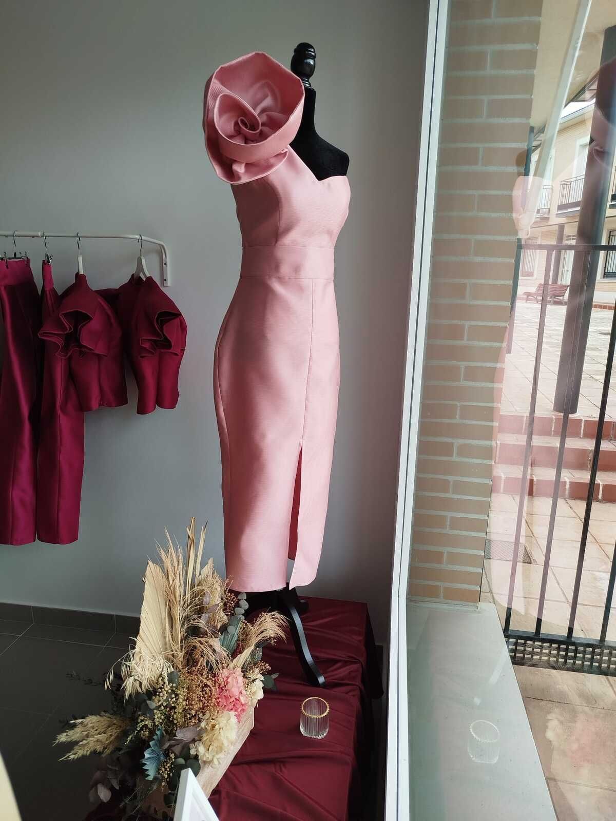 Vestido rosa sobre maniquí con gran detalle en los hombros, en escaparate de una tienda.