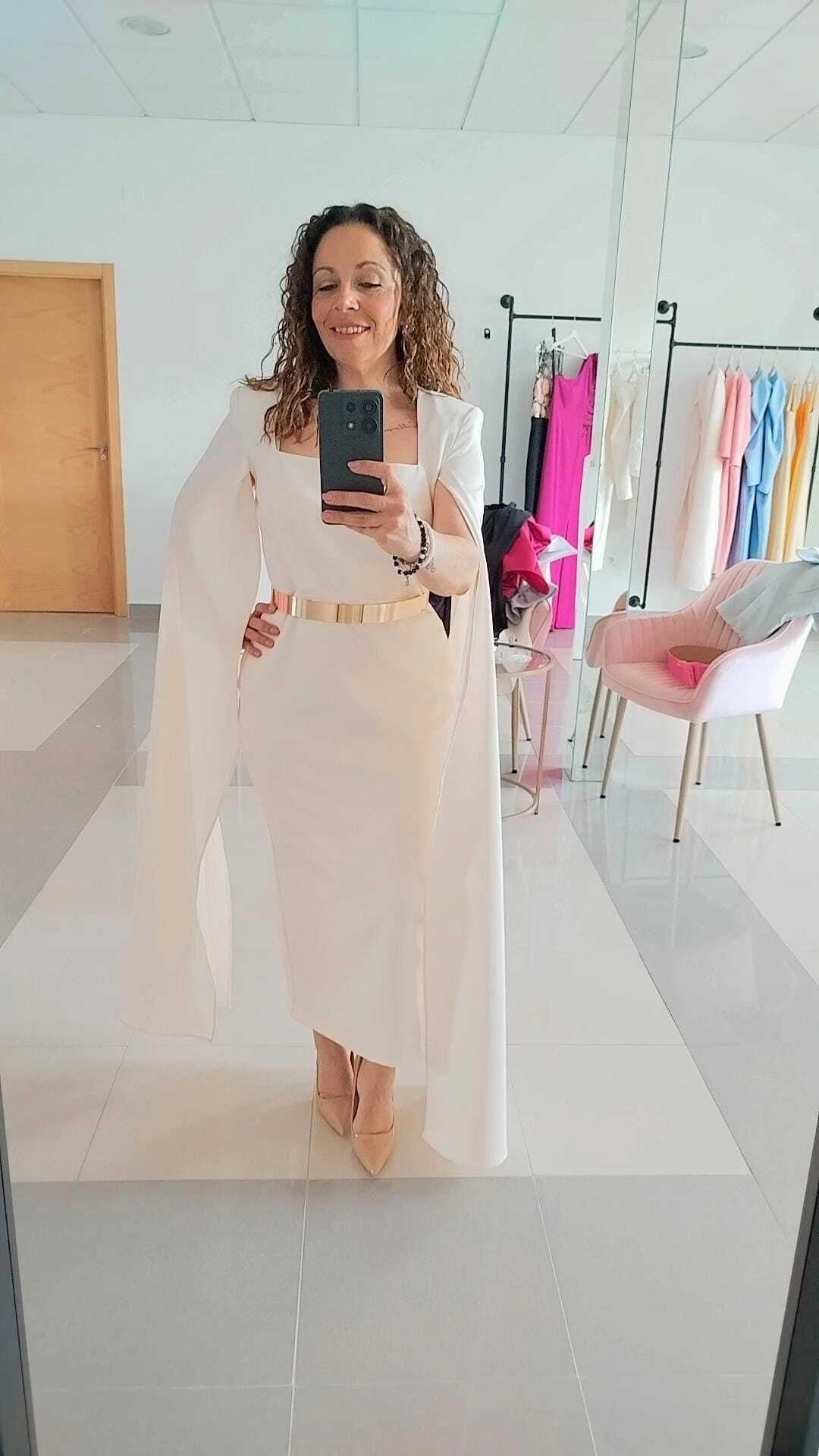 Mujer con vestido crema y cinturón dorado tomándose una selfie en una tienda.