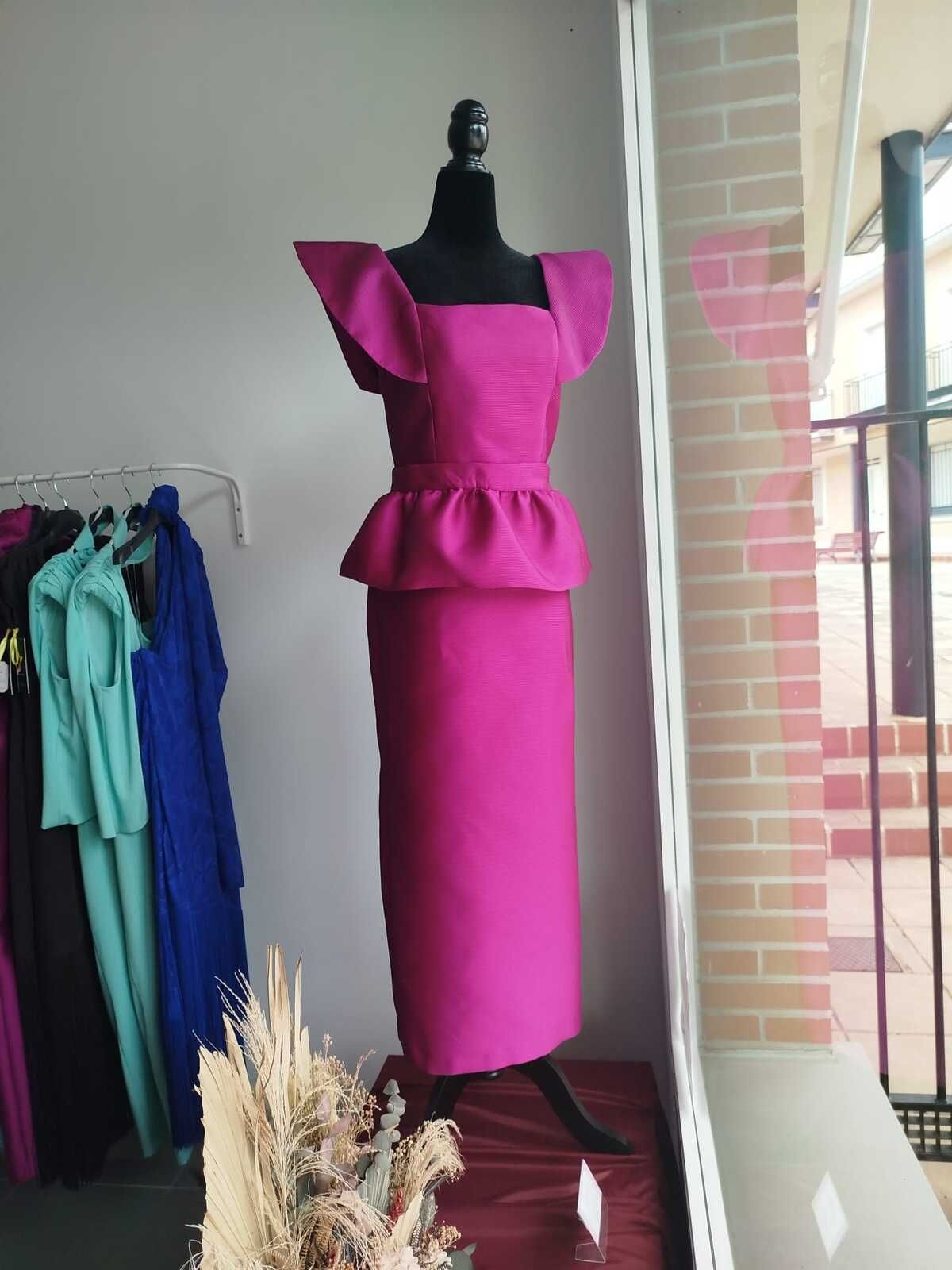 Un vestido magenta con escote cuadrado y peplum sobre un maniquí, expuesto en el escaparate de una tienda.
