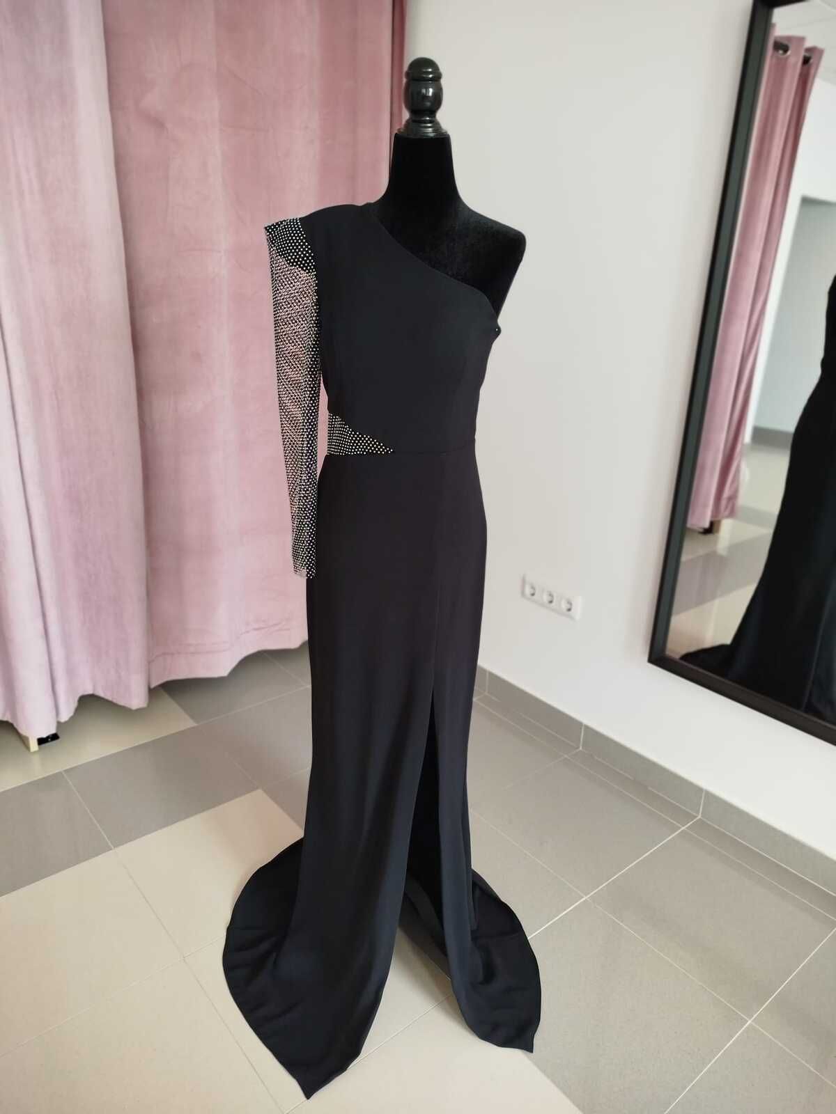 Vestido de noche negro de un solo hombro sobre un maniquí con manga joya, abertura hasta el muslo y cola.