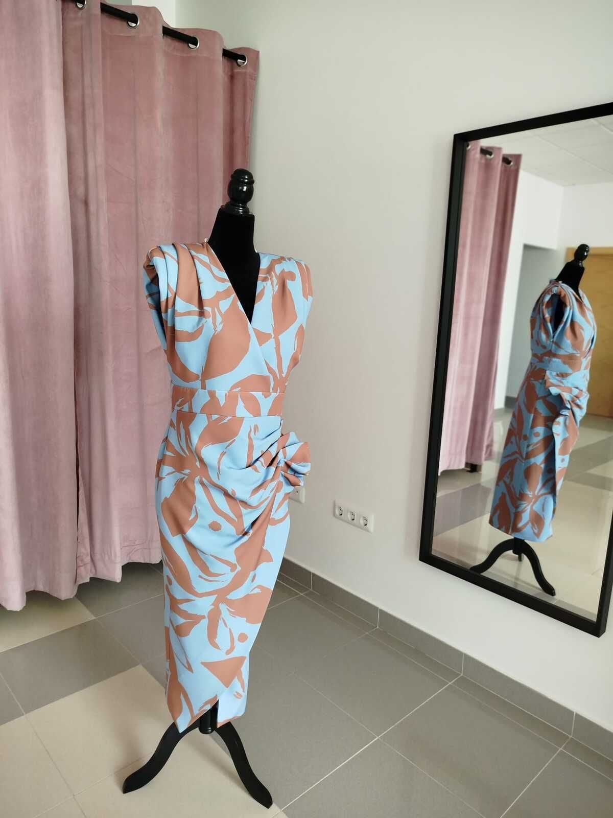 Vestido en un maniquí en una habitación; azul claro con estampado floral marrón, reflejado en un espejo cercano.