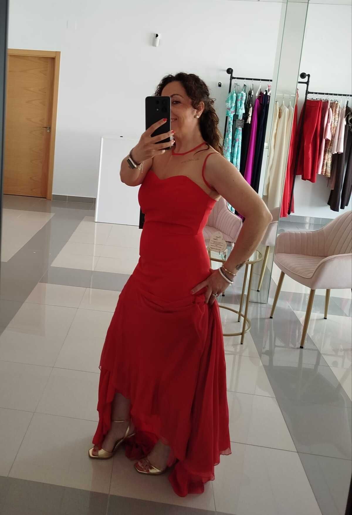 Mujer con un vestido formal rojo, posando frente a un espejo en una boutique.