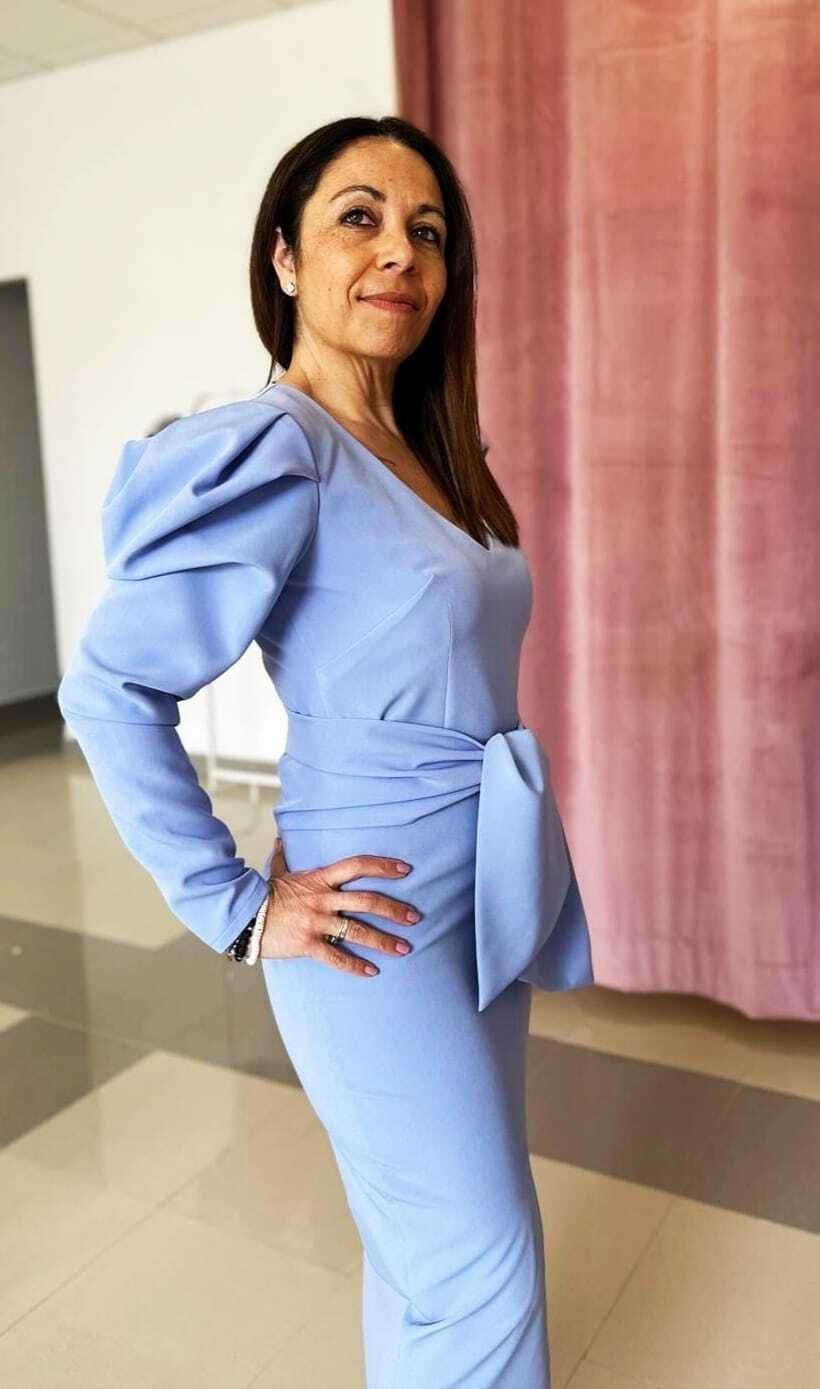 Mujer con vestido azul claro con mangas abullonadas, posando en el interior.