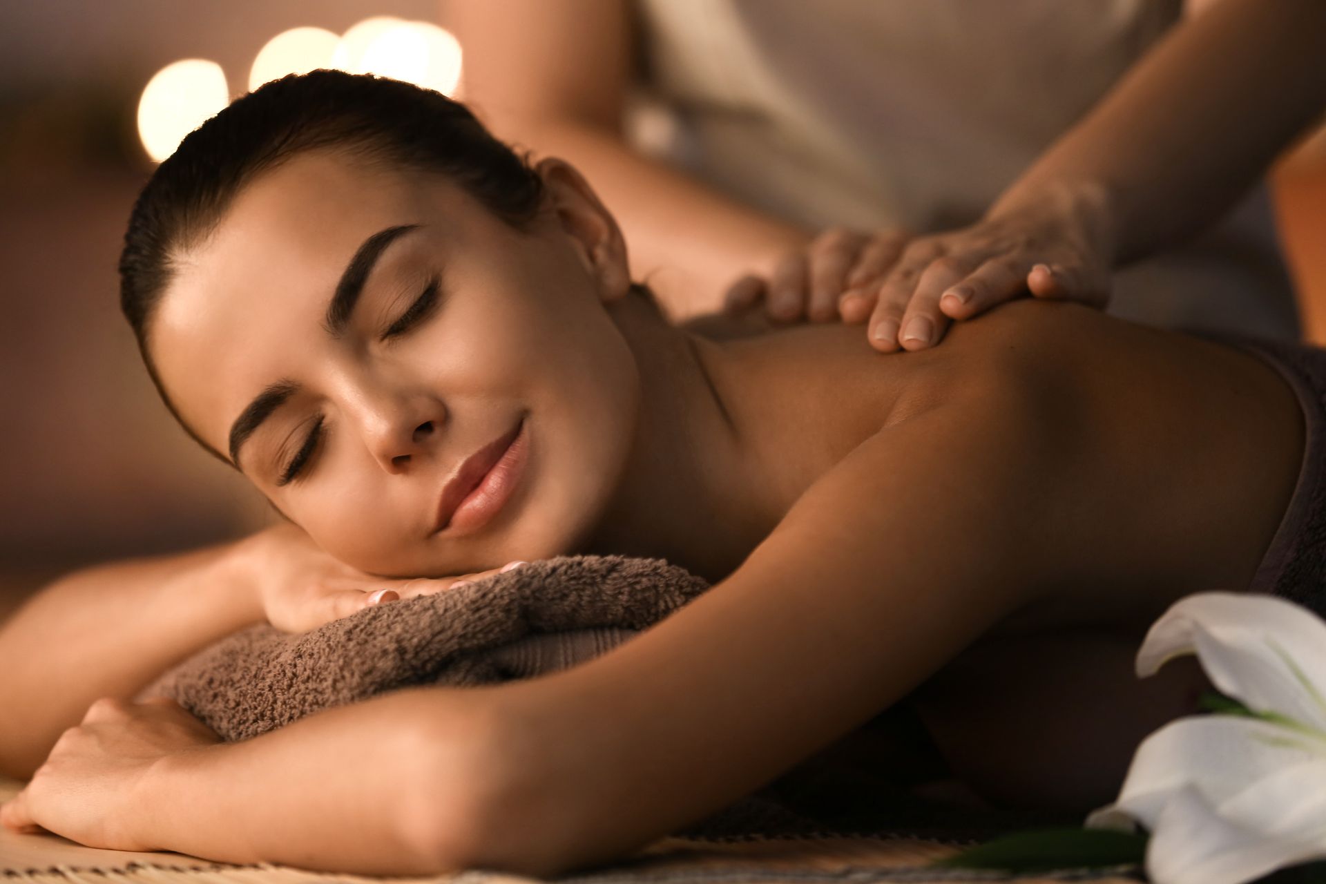 Une personne recevant un massage des épaules dans un spa chaleureux, les yeux fermés et détendue.
