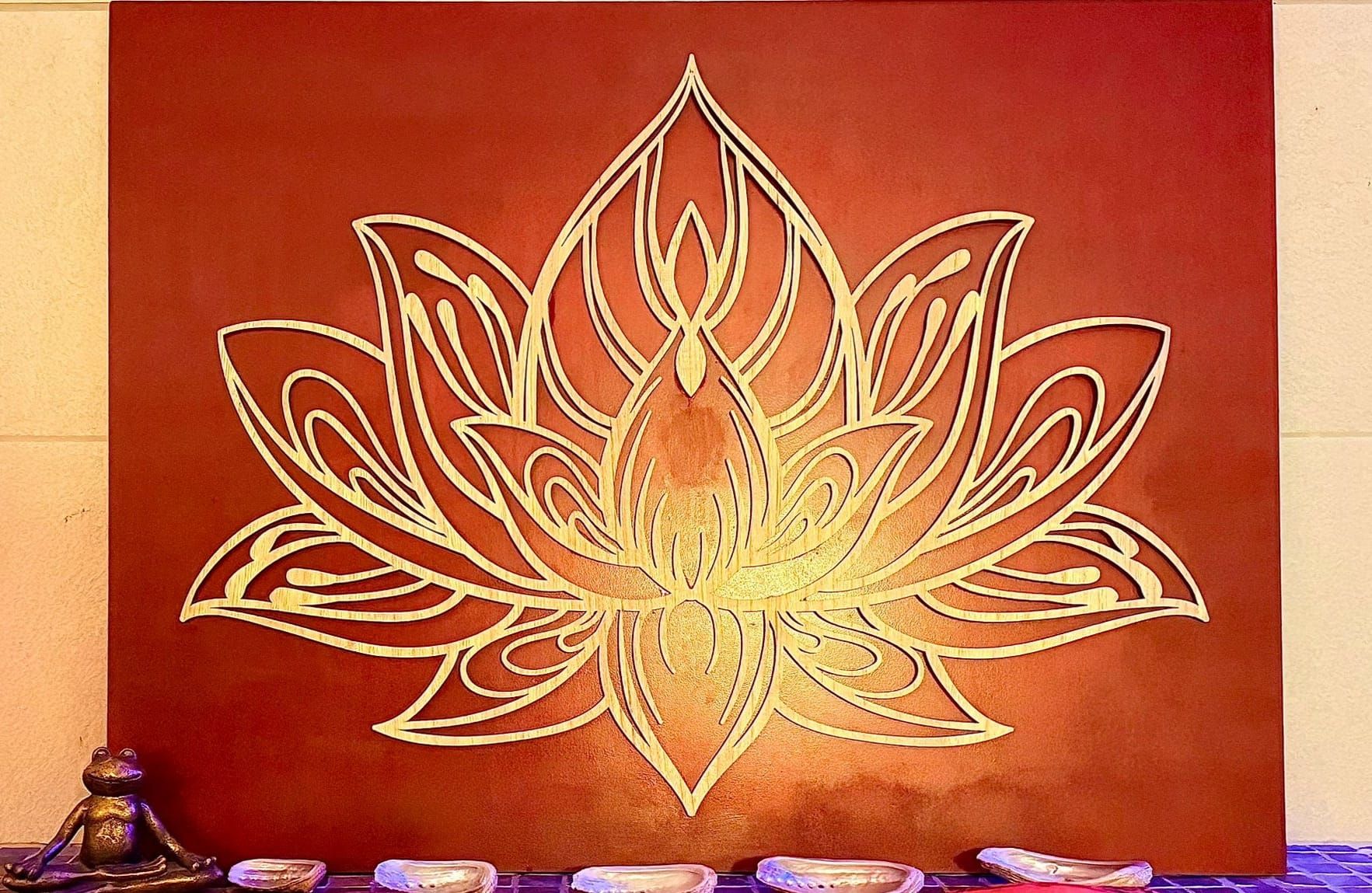 Peinture murale de lotus doré sur un mur rouge avec de petits objets décoratifs le long du bord inférieur