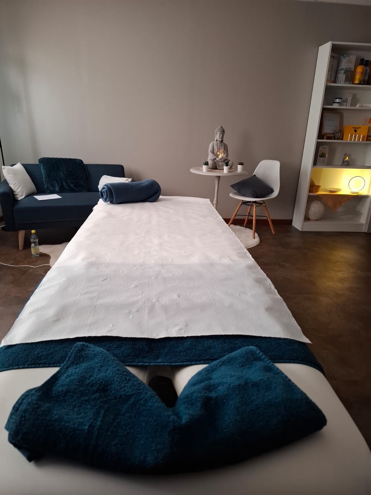 Table de massage dans une salle de spa avec une serviette pliée bleu foncé et une chaise à proximité