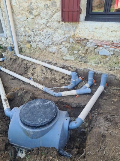 Filtre bleu pour piscine extérieure et tuyaux blancs dans une zone creusée à côté d'un mur de maison.