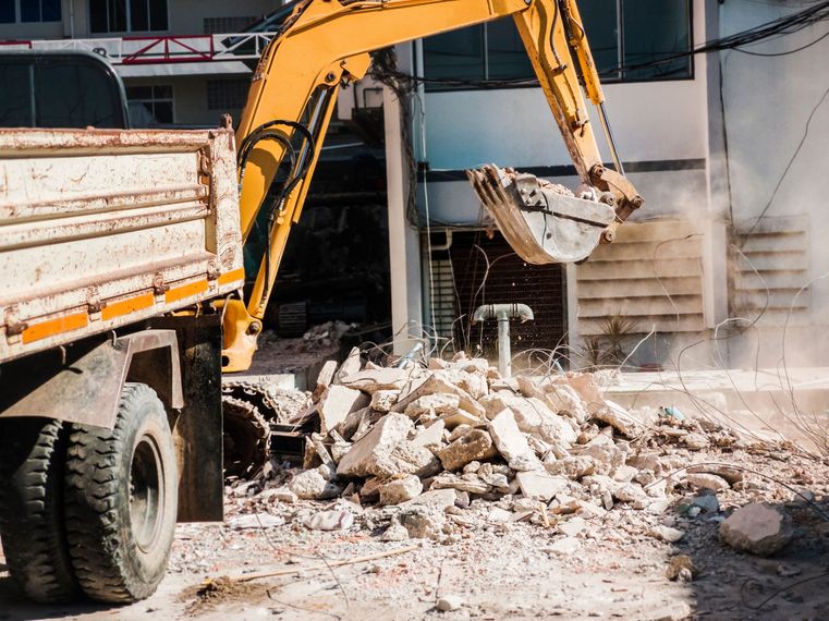 Une excavatrice démolit des gravats de béton à côté d'un camion sur un chantier de construction.