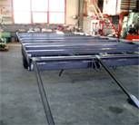 Anhängergestell mit ausgefahrenen Rampen in einer Werkstatt. Graues Metall, Betonboden, Fenster im Hintergrund.