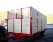 Roter landwirtschaftlicher Anhänger mit Holzseitenwänden, im Freien geparkt.