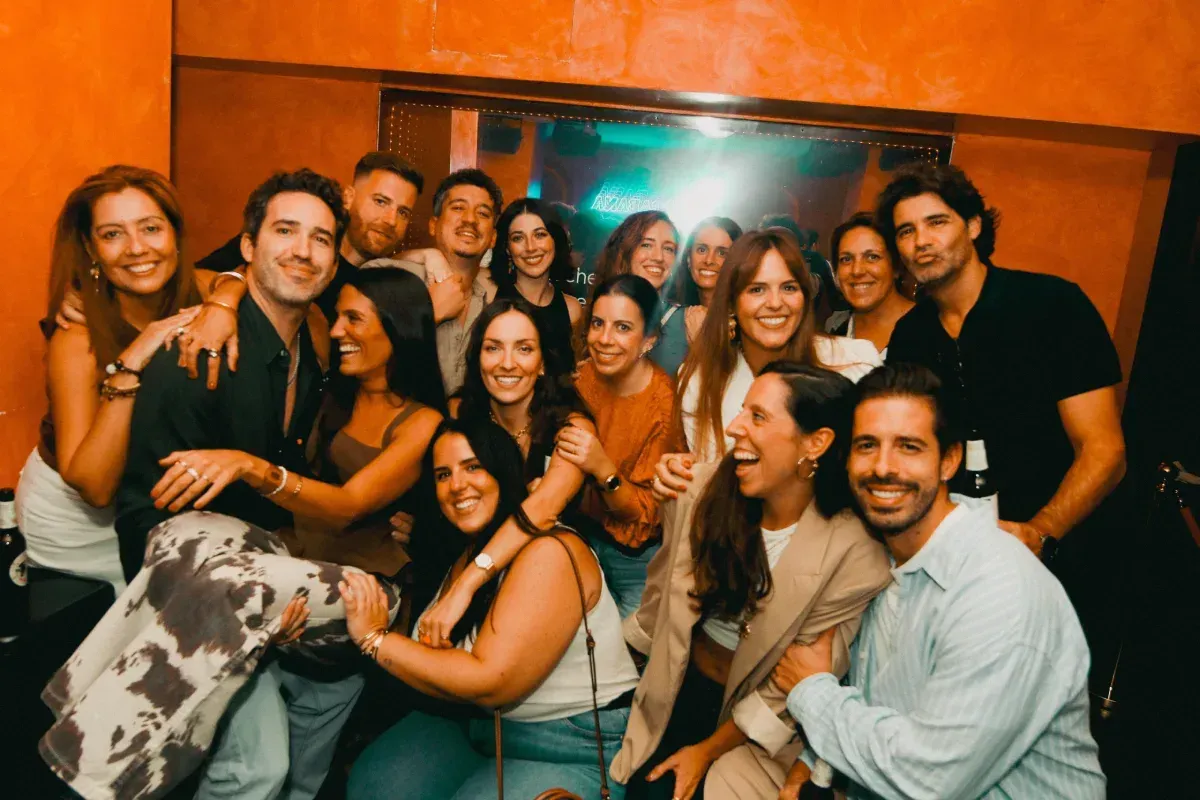 Grupo de personas sonriendo y abrazándose en un ambiente con poca luz.