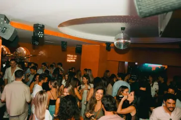 Fotografía en blanco y negro de una persona con los brazos en alto en un club abarrotado. 