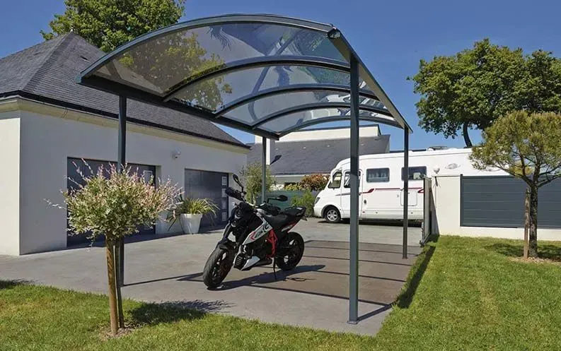 Une moto garée sous un abri de voiture en verre.