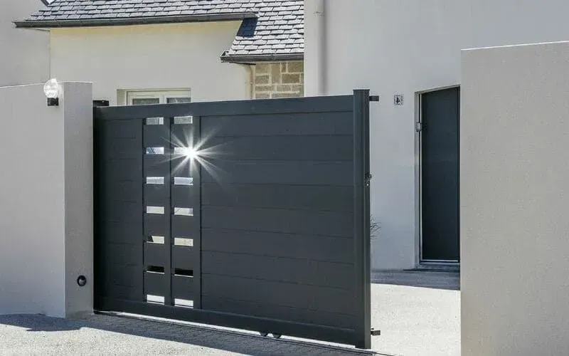 Portail coulissant moderne noir devant une maison gris clair, avec un portillon sur le côté.