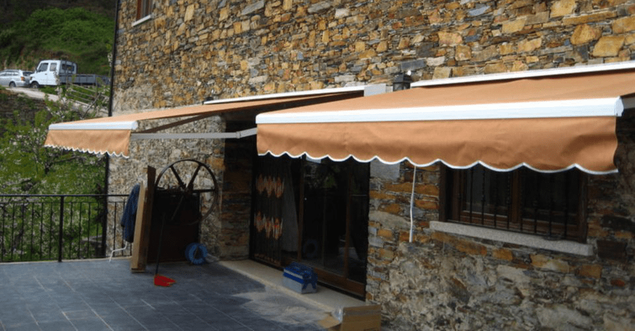 Toldos marrons sobre as janelas e portas de um edifício de pedra, proporcionando sombra.